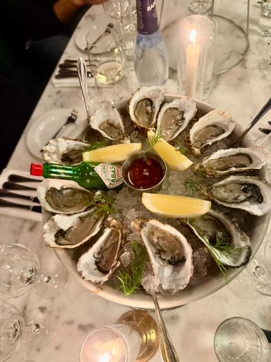 Tallrik med ostron, citronklyftor och en flaska sås i mitten.